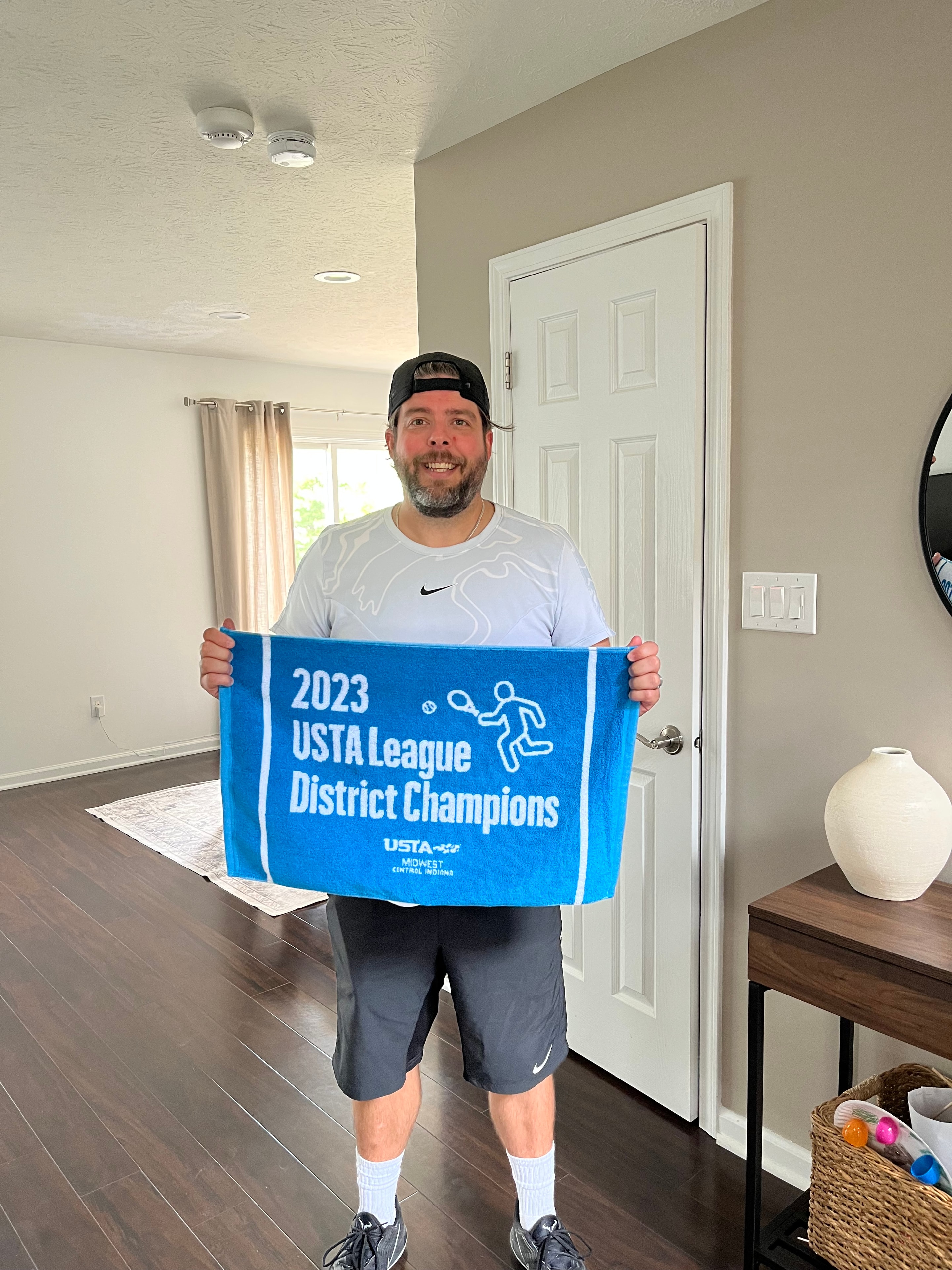 Coach Justin holding his 2023 USTA League District Champions towel