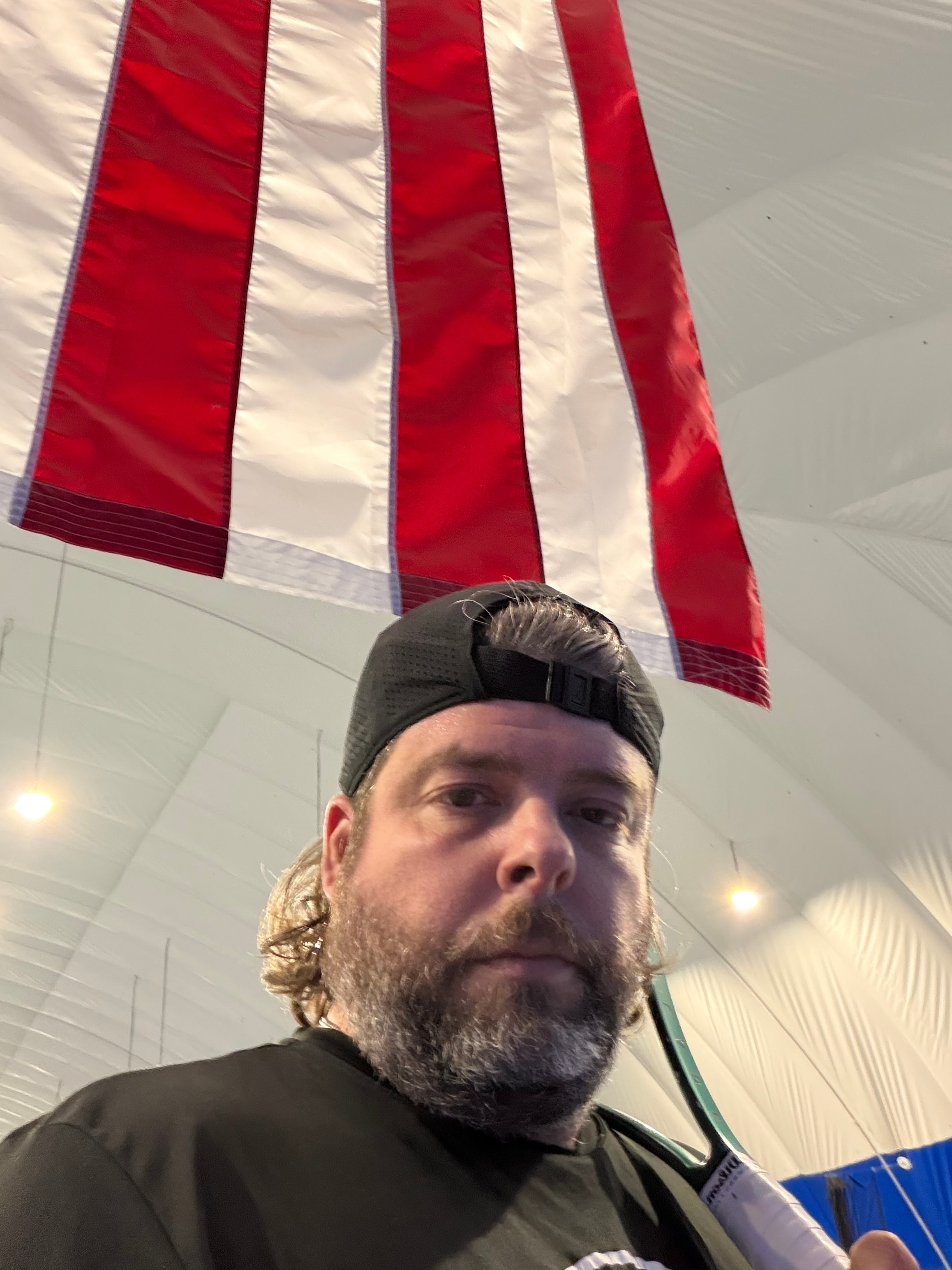Coach Justin inside an indoor tennis facility with an American flag overhead